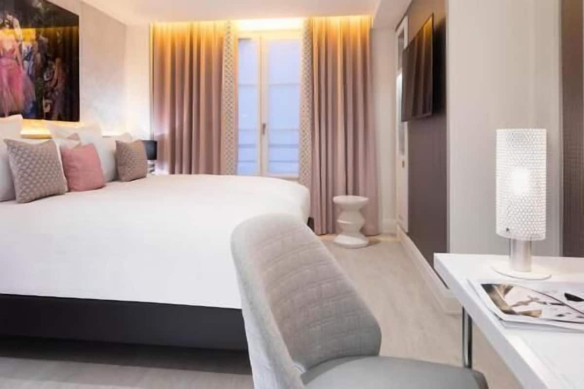 Habitació d'hotel moderna amb un llit gran, una taula de nit amb una làmpada, una taula auxiliar i una cadira.