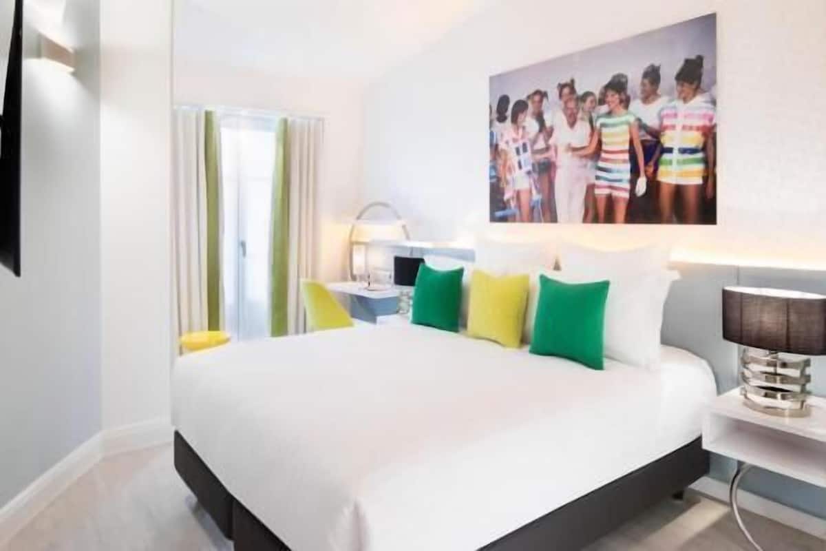 Una habitació d'hotel moderna amb un llit gran, una taula de nit, una làmpada i un quadre a la paret.