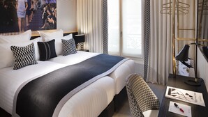 A hotel room with a large bed, a desk with a lamp, a chair, and a window with curtains. - Hôtel Dress Code (Paris)