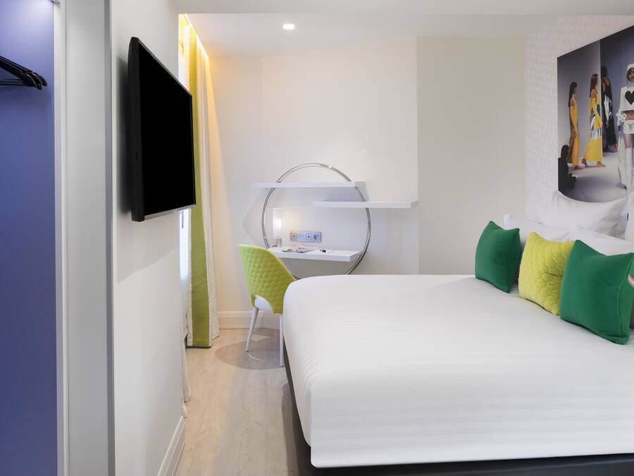 Una habitación de hotel moderna con una cama, un escritorio, una silla, un televisor y un espejo.