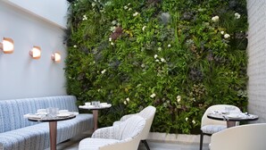 A modern indoor seating area with a vertical garden wall, cushioned seating, and round tables. - Hôtel Dress Code (Paris)