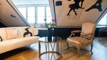 Een moderne woonkamer met een bank, een ronde tafel met een bloevas, en een klassieke fauteuil.
