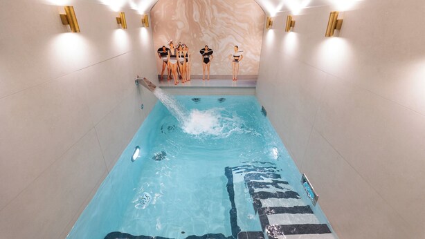 A swimming pool with a marble wall and gold wall sconces. - Hôtel Dress Code (Paris)