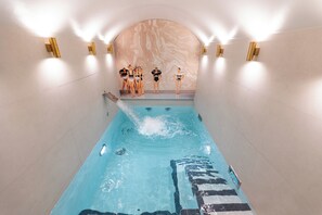 A swimming pool with a marble wall and gold wall sconces. - Hôtel Dress Code (Paris)