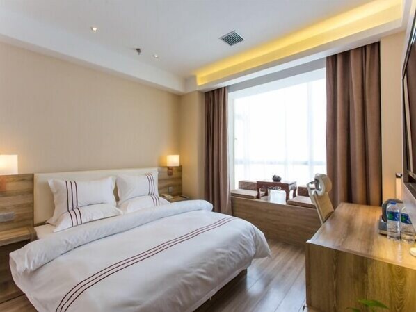 Habitación de hotel con una cama grande, un escritorio de madera y vistas a la ciudad a través de amplias ventanas.