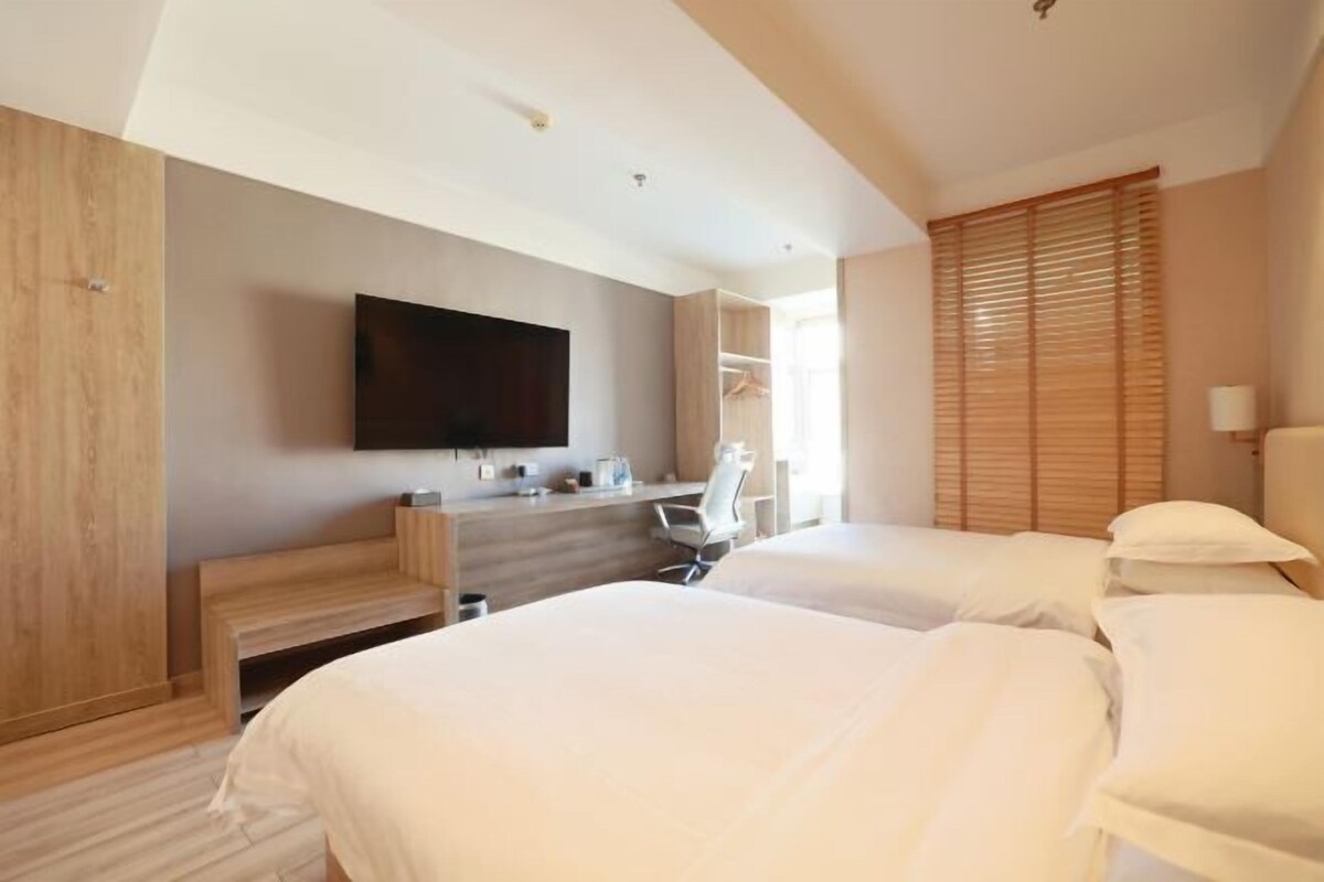 A hotel room with two beds, a desk, a chair, a TV, and a wardrobe.