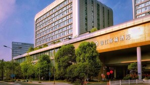 Un hôtel moderne, avec une enseigne bien visible en caractères chinois, plusieurs étages et un parking agrémenté d’arbres à l’avant.