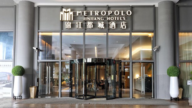 L’entrée de l’hôtel Metropole Jinjiang City, avec sa porte tournante et sa façade en verre.