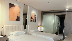 Une chambre d’hôtel avec deux lits, une table de chevet avec une lampe, une commode, un grand miroir et des œuvres d’art accrochées au mur.