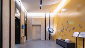 Un hall d’hôtel moderne au design minimaliste, comprenant un comptoir d’accueil, un grand lampadaire et un mur orné de tableaux encadrés.