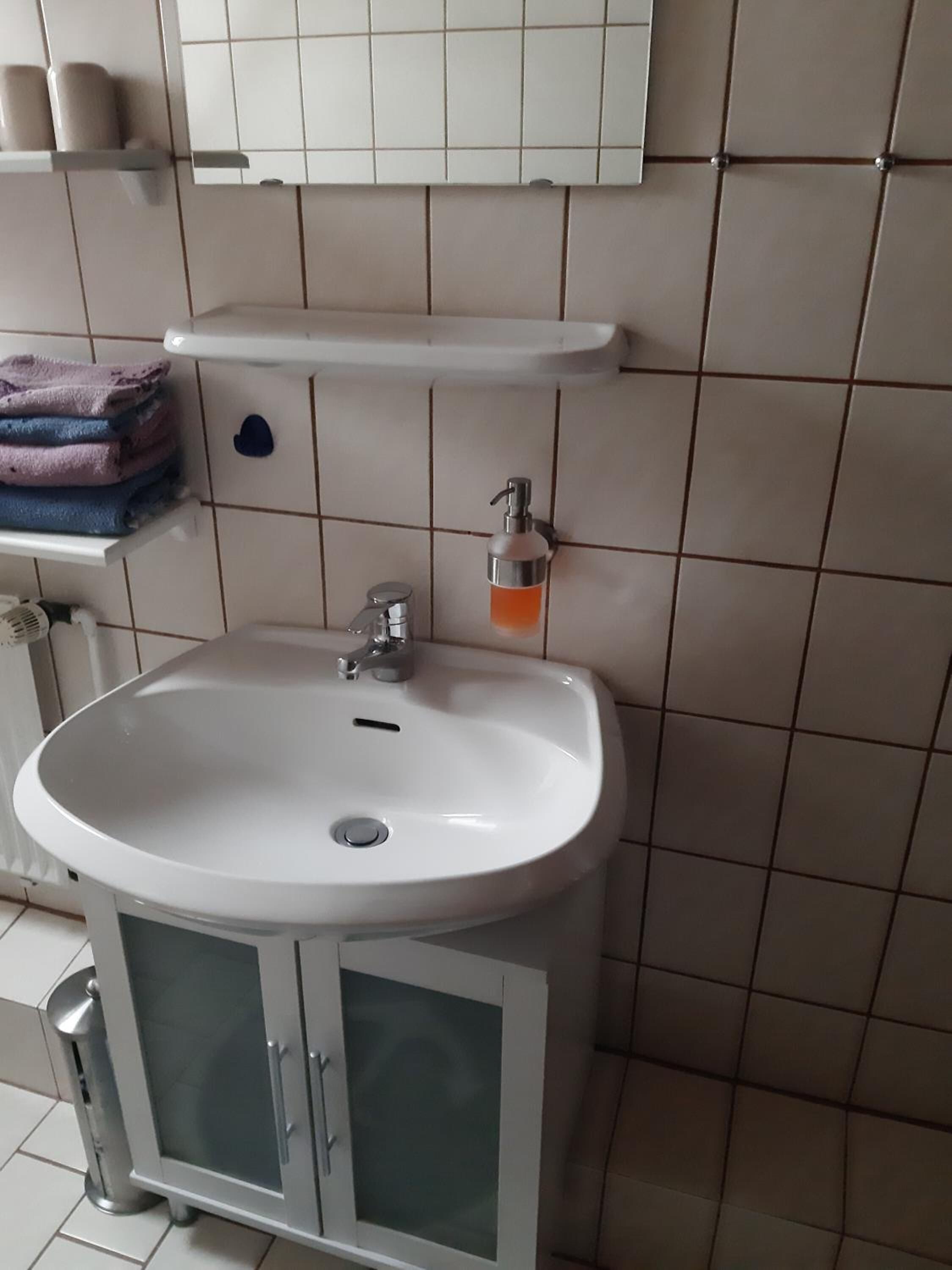 A bathroom with a white sink, a mirror above it, and a towel rack with folded towels.