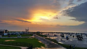 A coastal area with a long pier extending into the water, surrounded by grassy areas and industrial structures.