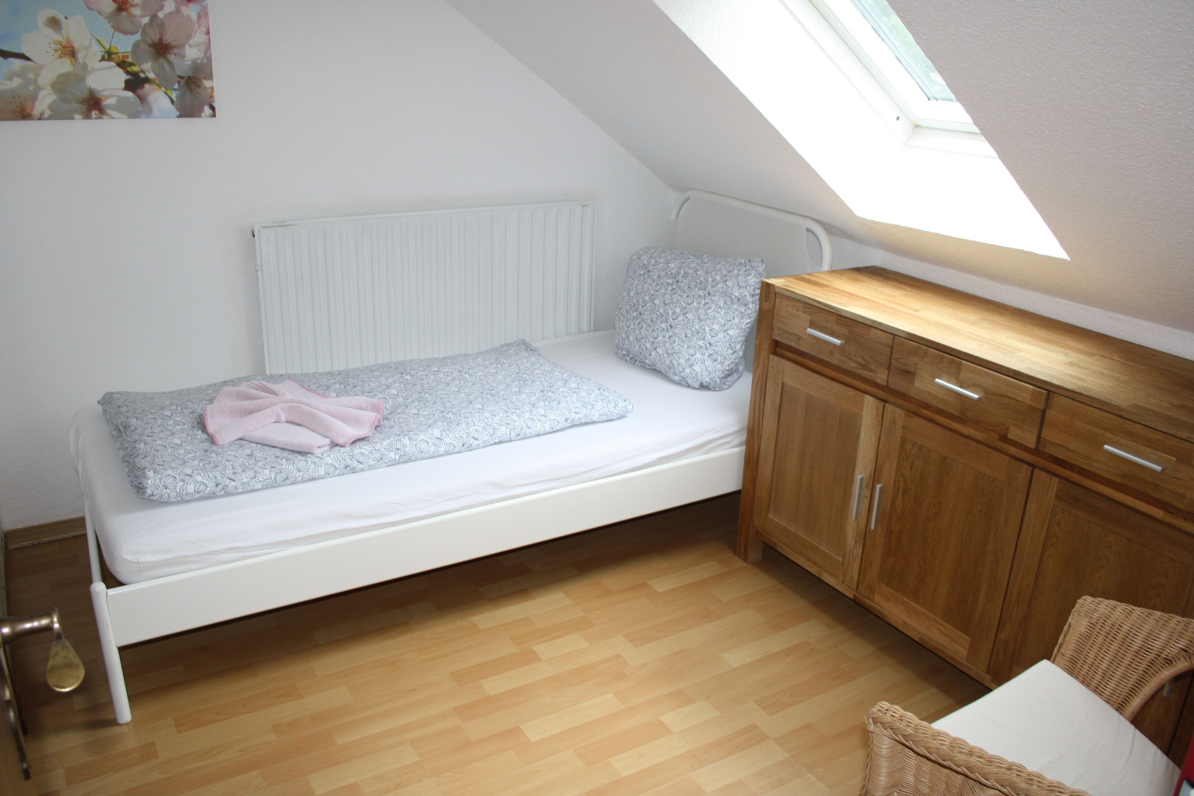 Een kleine kamer met een enkel bed, schuine kap en dakraam.