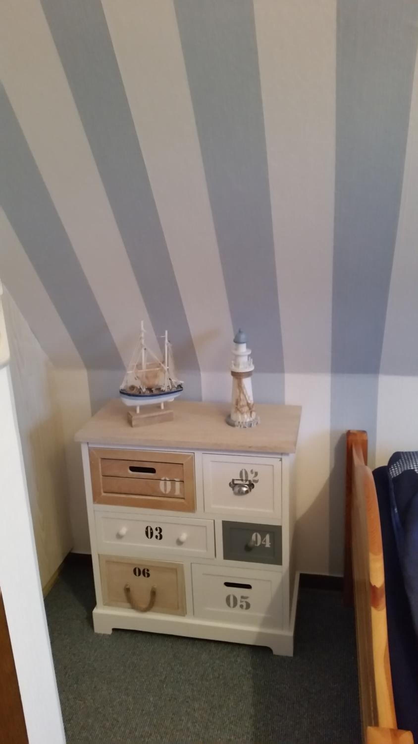 A small white dresser with drawers numbered 01 to 06, a ship model, and a lighthouse model on top.