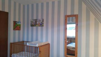 A room with striped walls, a crib, a bed, and a mirror reflecting a window.