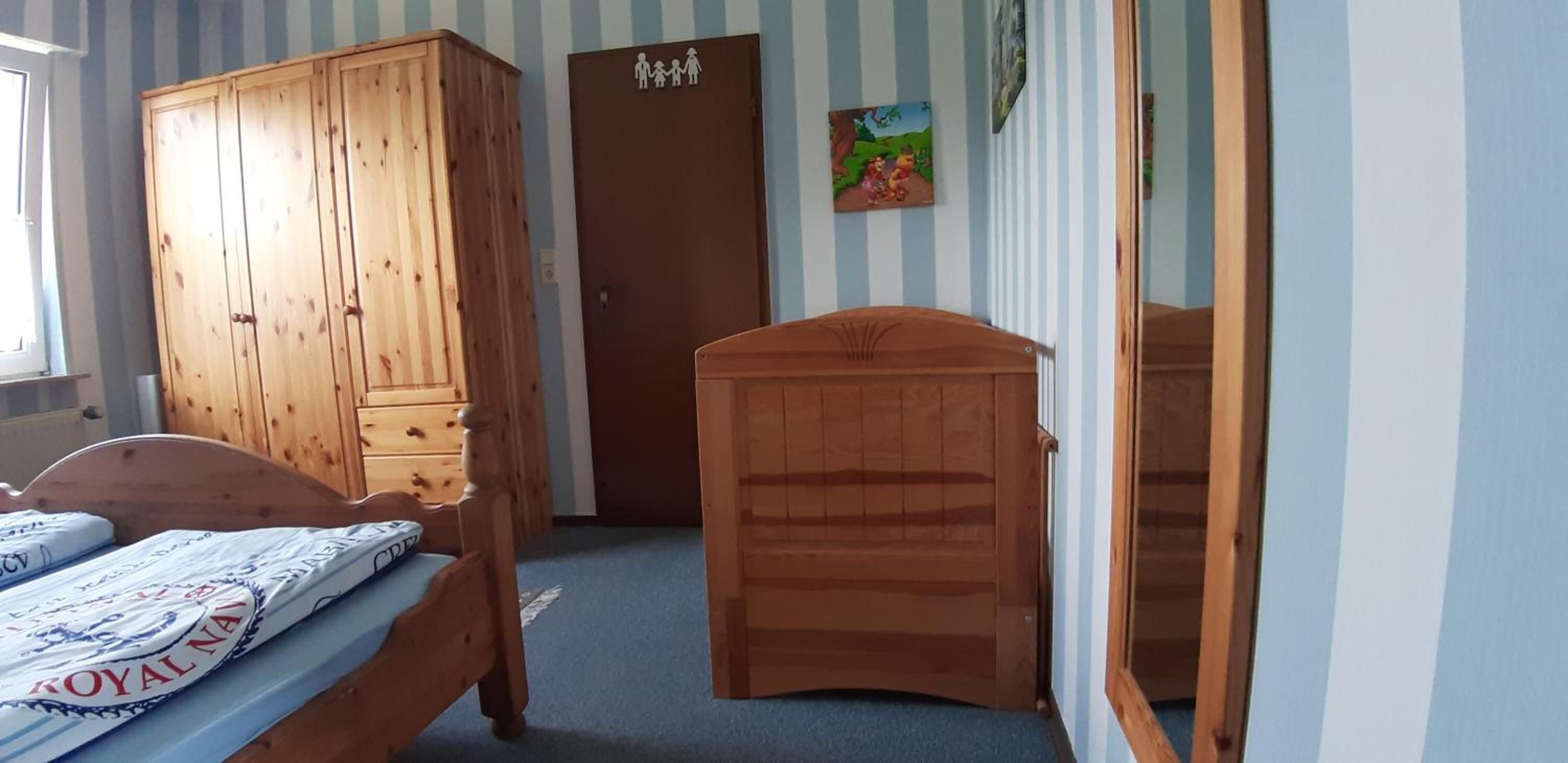 A room with a wooden bed, a wardrobe, a door with a family symbol, and a wall with a children's painting.