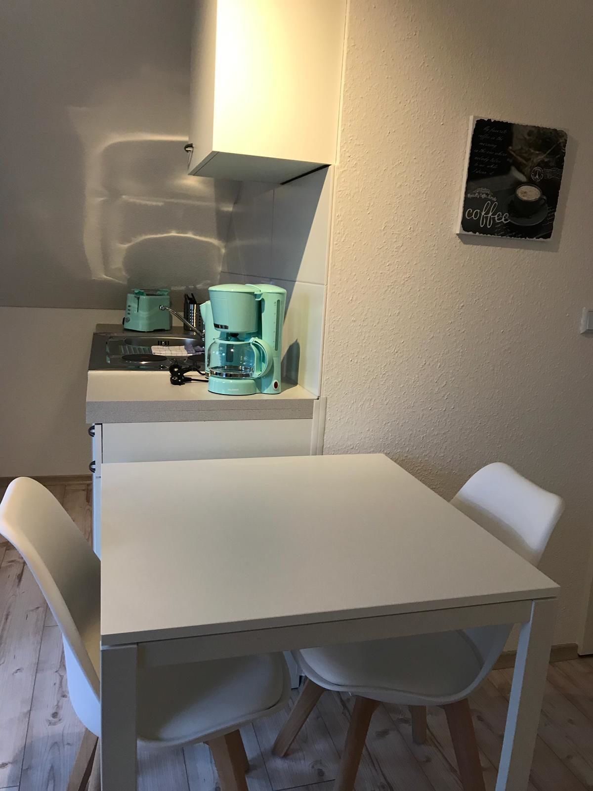 A small kitchenette with a coffee maker, a sink, and a white table with two chairs.