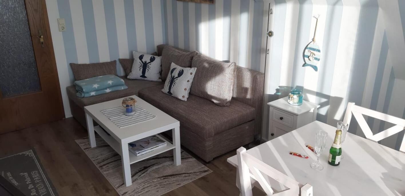 A cozy living room with a brown sofa, striped curtains, a white coffee table, and a small white table with a bottle and glasses.