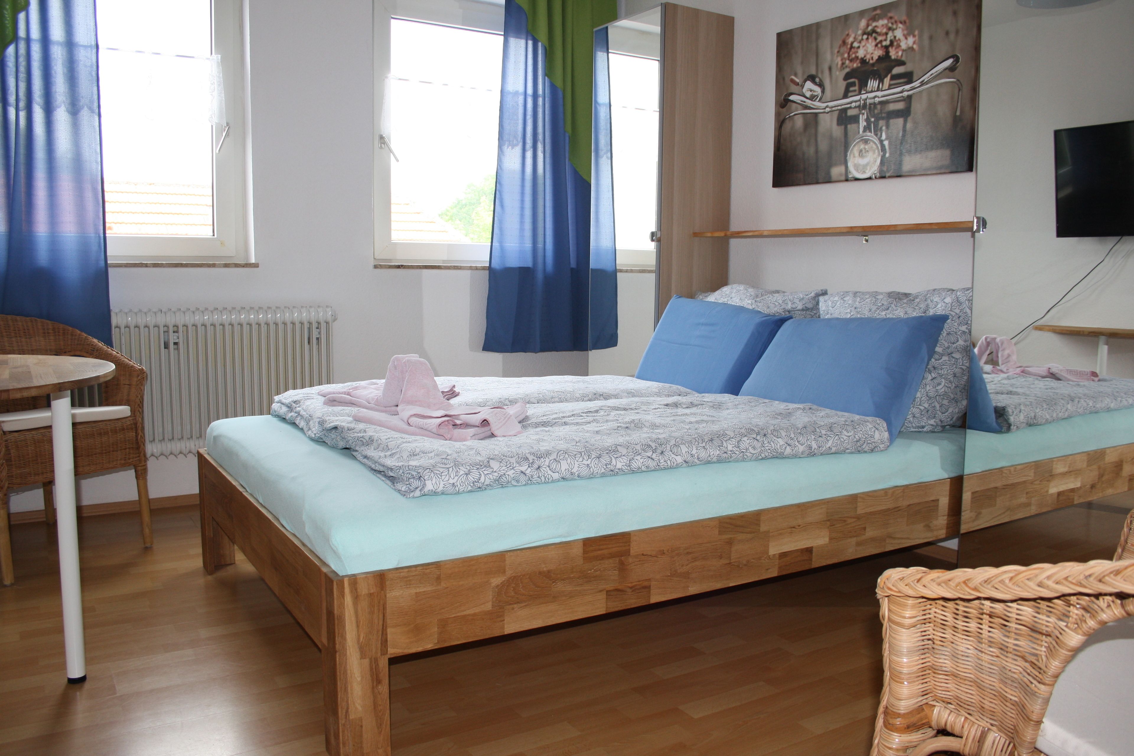 A bedroom with a wooden bed, a wicker chair, a table, and a radiator.