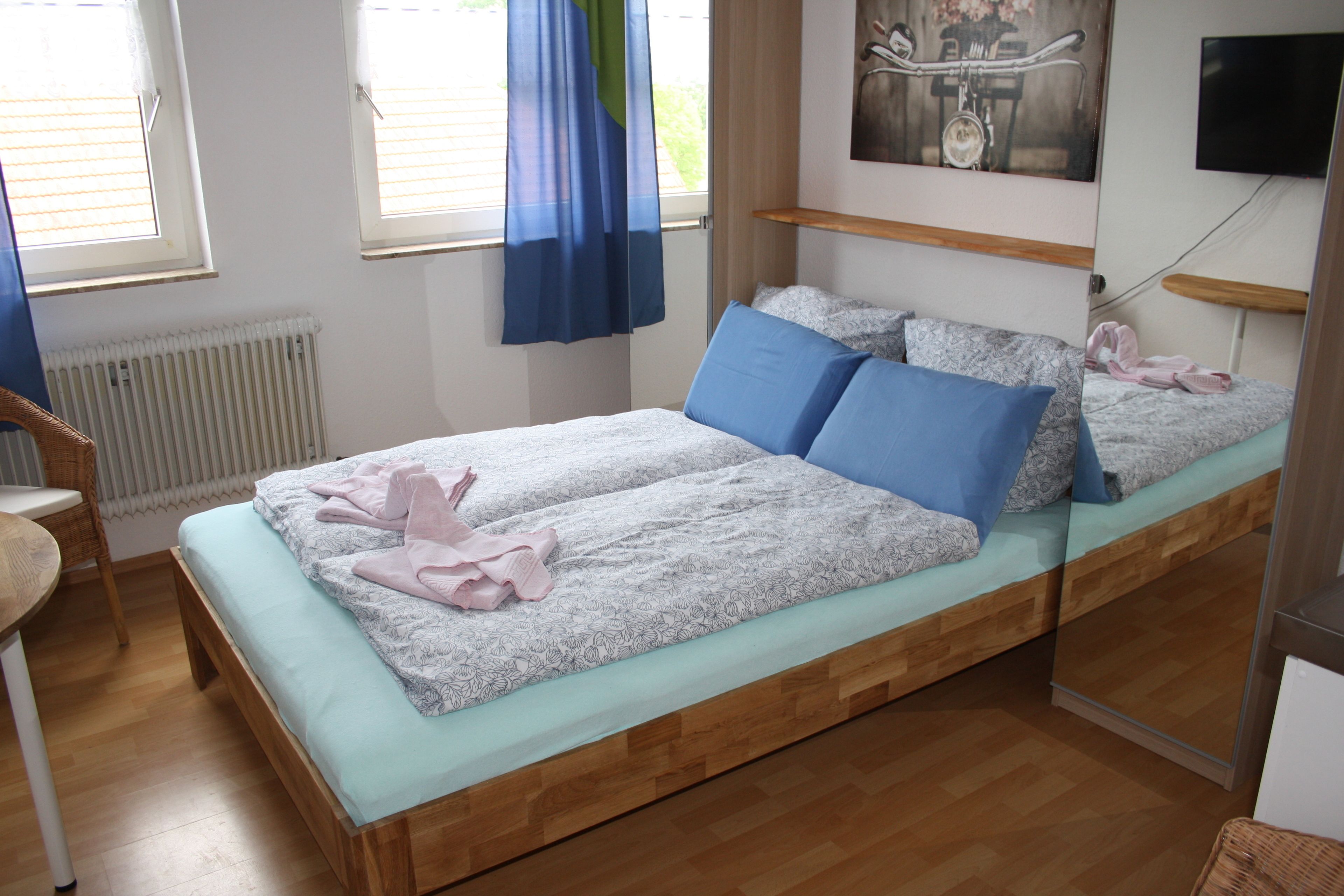A bedroom with a bed, pillows, a chair, a radiator, and a television on the wall.