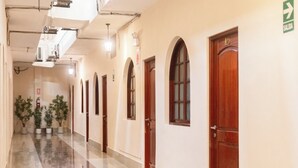Een lange, glanzende hal met houten deuren en boogvensters, die leidt naar verschillende kamers.
