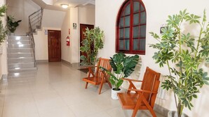 Een hotel lobby met een trap, houten stoelen, potplanten en een groot rondboogvenster.