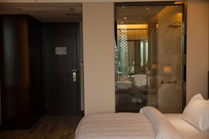 Une chambre d’hôtel avec un lit, une douche fermée par des parois de verre et une porte sombre.