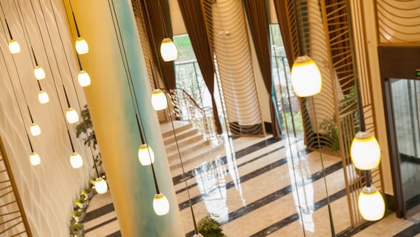 Un hall d’hôtel avec des luminaires suspendus, un escalier et une vue sur l’extérieur.