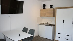 Una cocina compacta con zona de comedor, un televisor montado en la pared y una cafetera en el mueble.