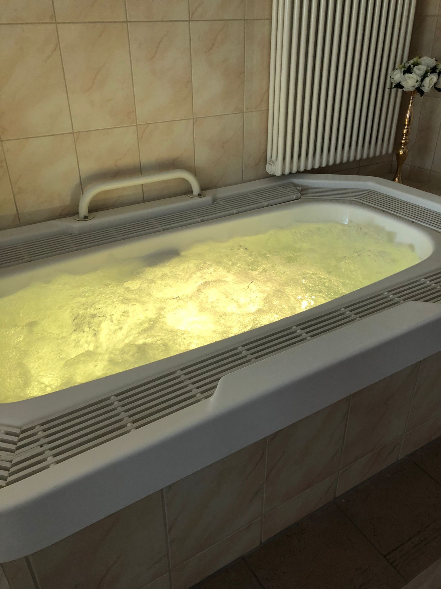 Eine Badewanne mit weißem Innenraum, einer Handstange und einem Heizkörper darüber.