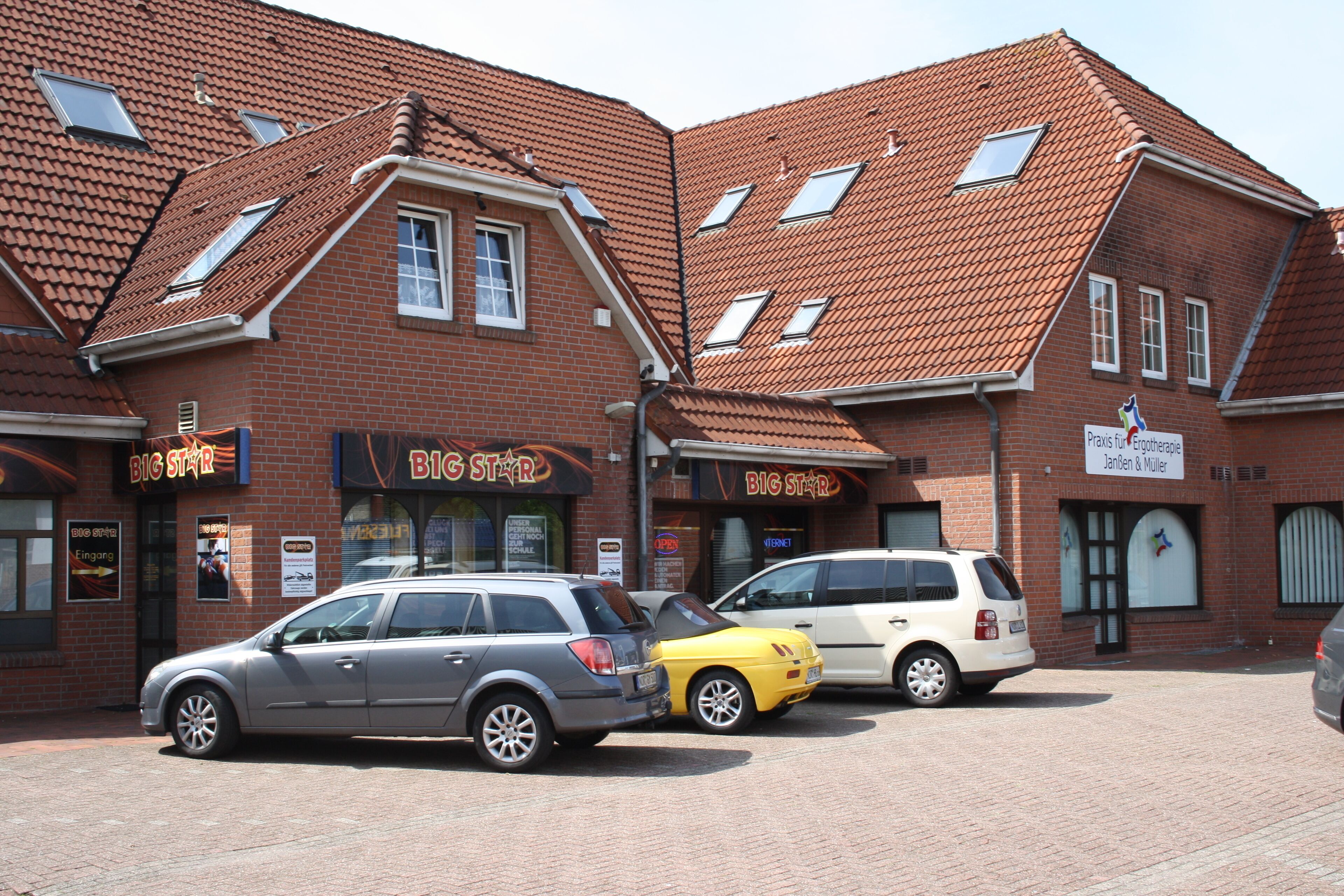 A building with multiple storefronts, including 'Big Star' and 'Pravis'. There are parked cars in front.