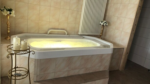 Un baño con bañera, tocador con espejo, y una pequeña mesa con velas y flores.
