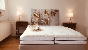 Un dormitorio con una cama, dos mesitas de noche con lámparas, un radiador y una pared decorada con motivos florales.