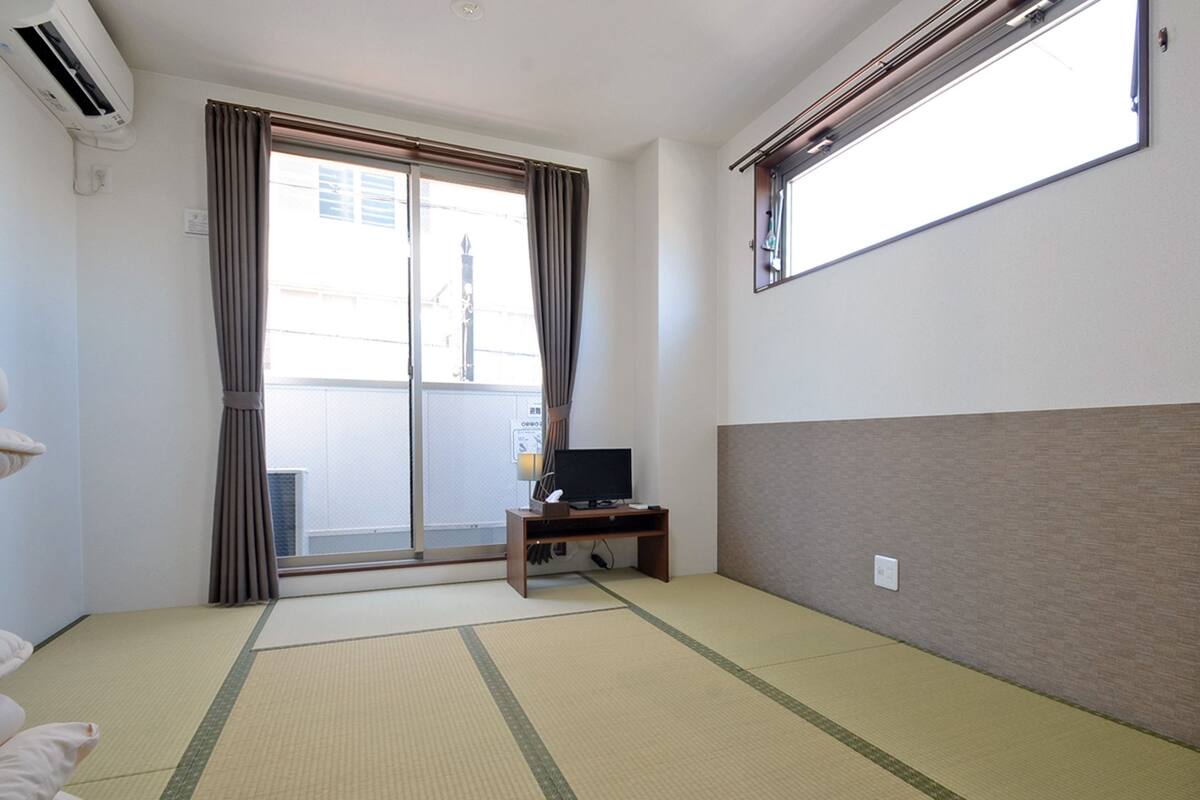A room with tatami flooring, a sliding glass door, a desk with a computer, and a window with blinds.