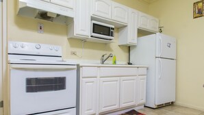 A kitchen with white cabinets, a stove, a microwave, and a refrigerator. - Winchester Estate (Kingston)