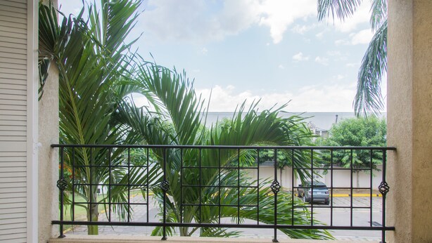 A balcony with a metal railing, potted plants, and a view of a street with cars and buildings. - Winchester Estate (Kingston)