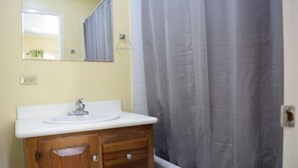 A bathroom with a wooden vanity, a white sink, and a shower curtain. - Winchester Estate (Kingston)