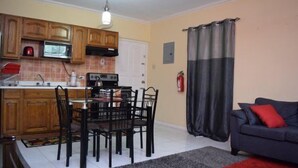 A compact kitchen with wooden cabinets, a microwave, and a dining area with a table and chairs. - Winchester Estate (Kingston)