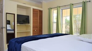 A bedroom with a bed, a television on a shelf, a wardrobe, and green curtains. - Winchester Estate (Kingston)