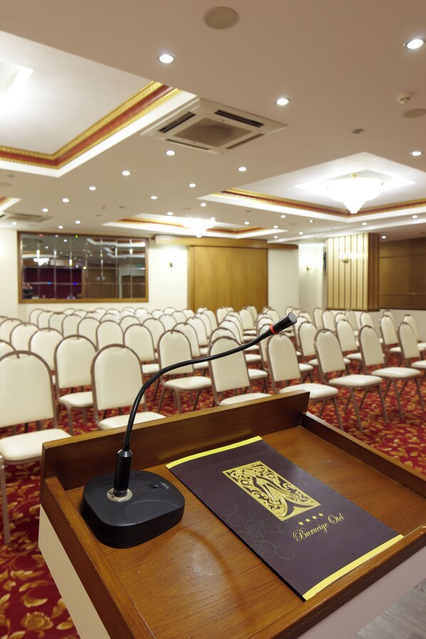 Un salón de conferencias con filas de sillas, un atril con un micrófono y una placa decorativa en el atril.
