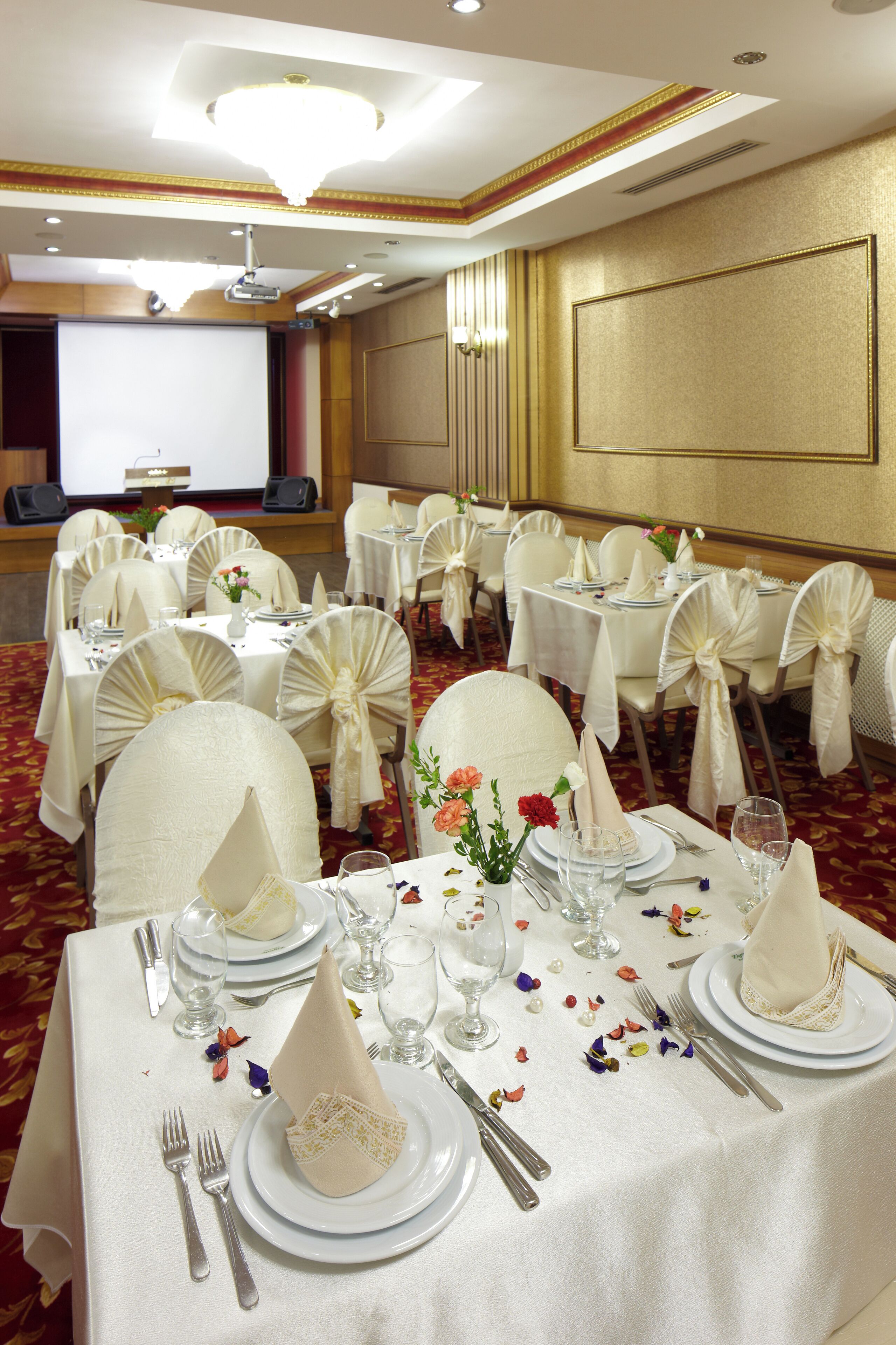 Une salle de banquet avec des tables rondes, des nappes blanches et des chaises ornées de rubans blancs.