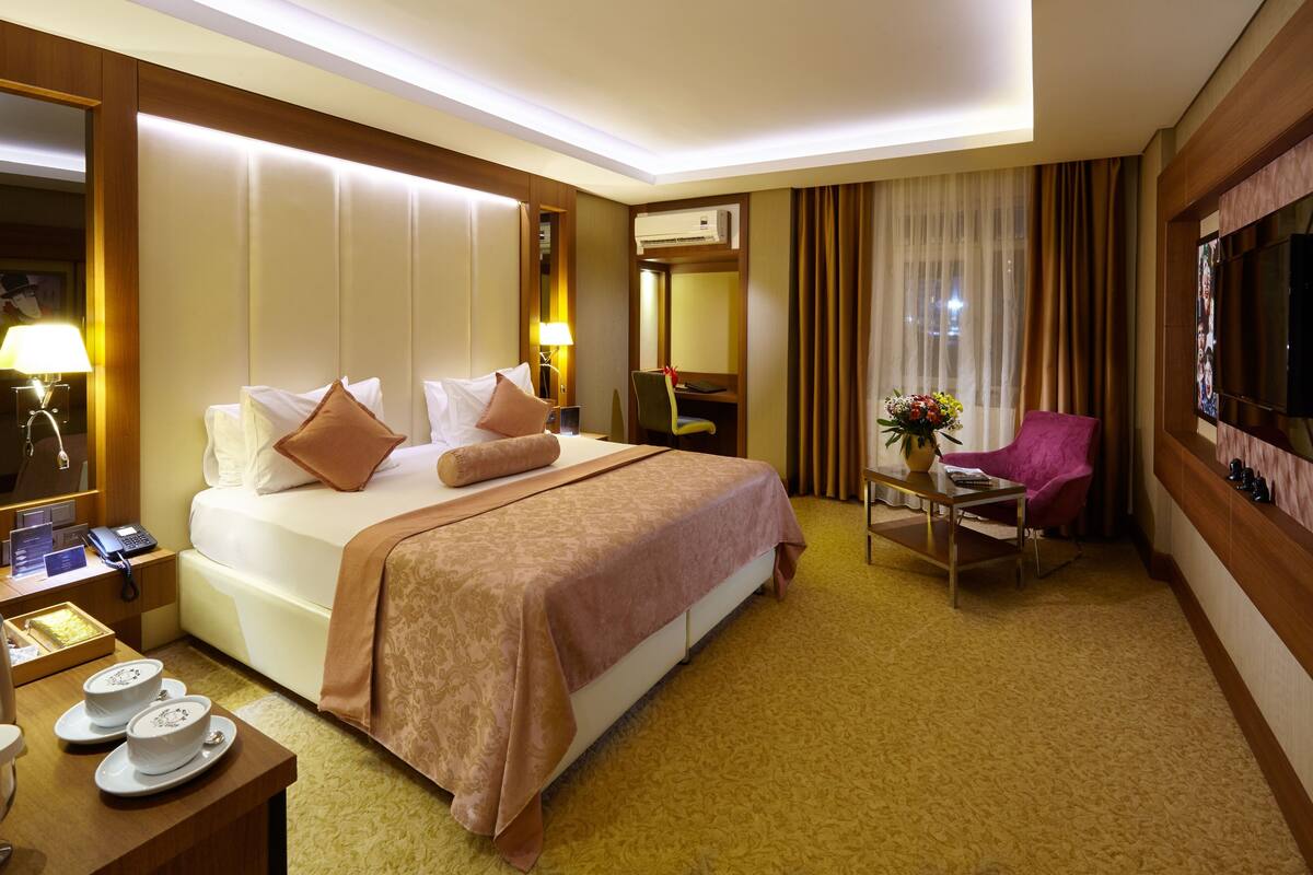Une chambre d’hôtel avec un grand lit, une table de chevet avec une lampe, une chaise, un téléviseur et un bureau avec un téléphone.