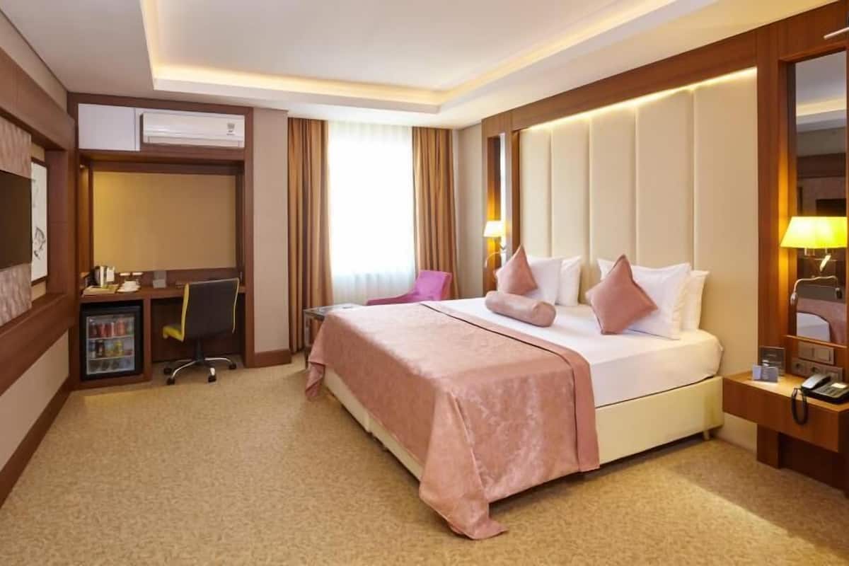 Une chambre d’hôtel équipée d’un lit, d’un bureau, d’une chaise, d’un mini-bar et d’une télévision.