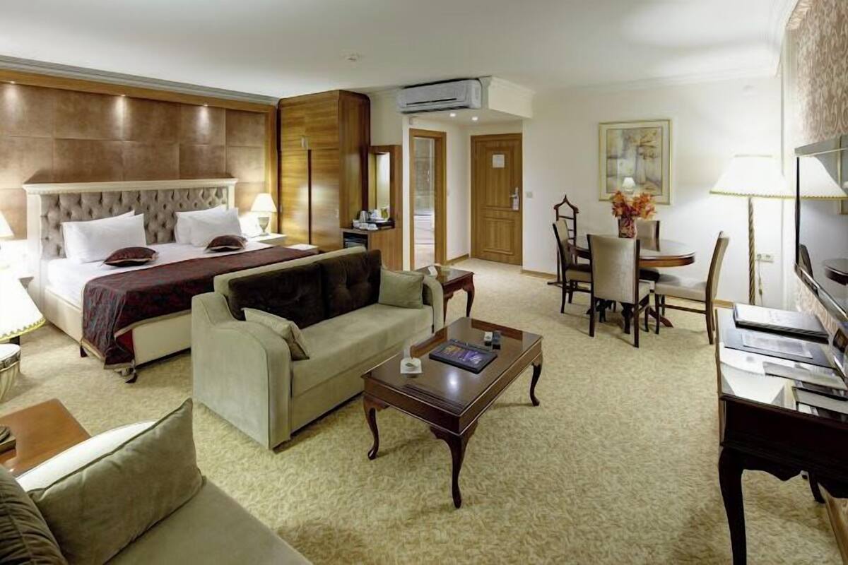 Une chambre d’hôtel avec un grand lit, un canapé, une table basse, une table à manger avec des chaises et un téléviseur.