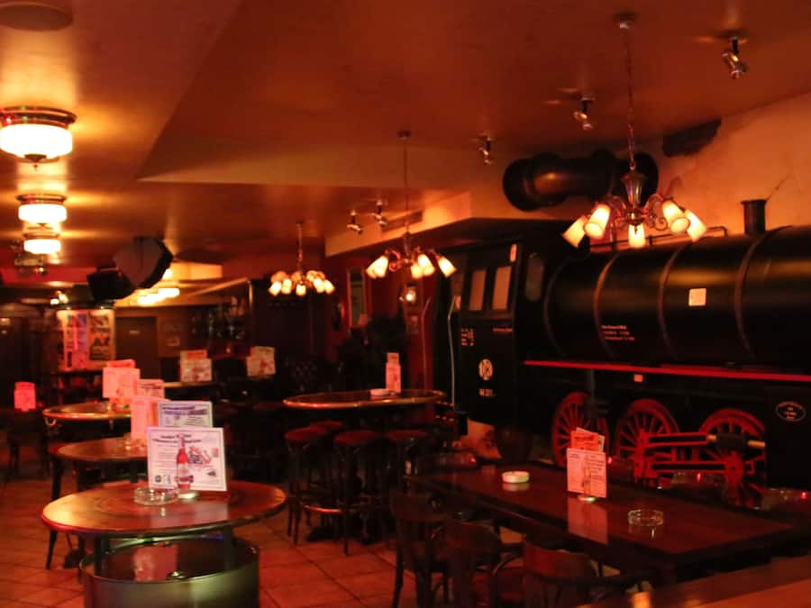 A dimly lit restaurant interior with wooden tables and chairs, hanging lights, and a vintage steam engine as a centerpiece.