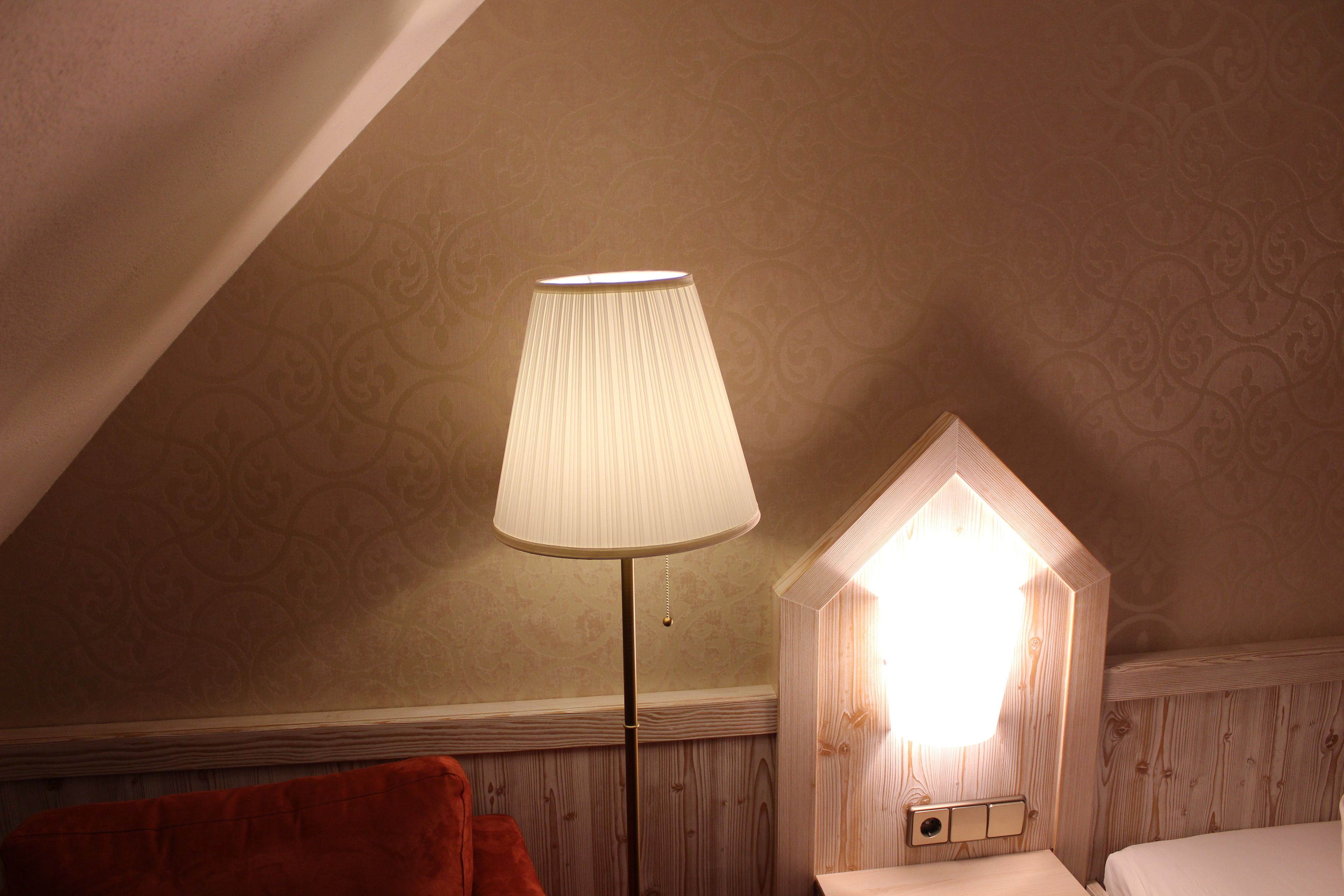 A room with a sloped ceiling, a floor lamp, a bed, and a wall-mounted light fixture.