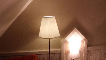 A room with a sloped ceiling, a floor lamp, a bed, and a wall-mounted light fixture.