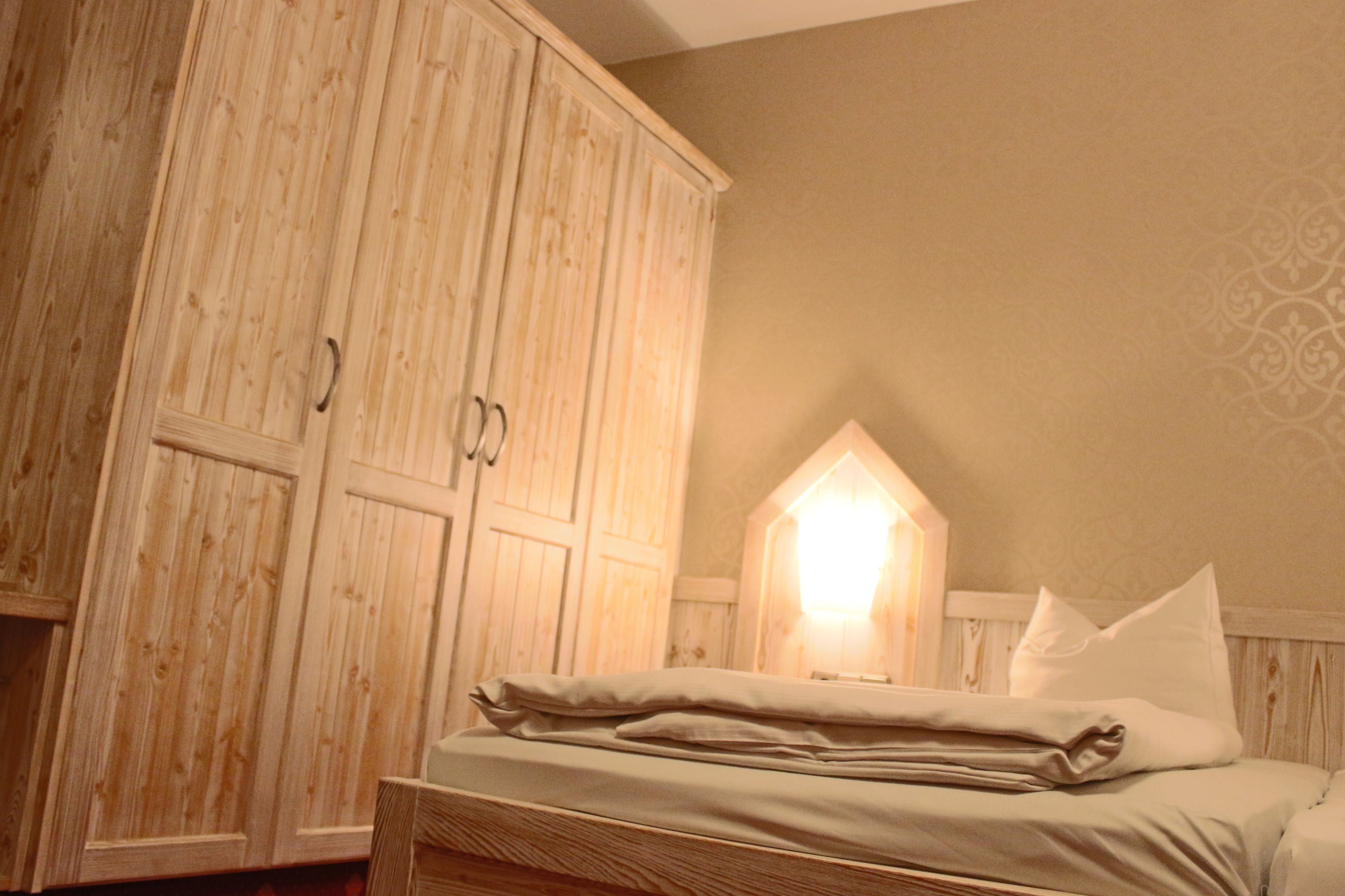 A bedroom with a wooden wardrobe, a bed with pillows, and a wall-mounted light fixture.