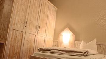 A bedroom with a wooden wardrobe, a bed with pillows, and a wall-mounted light fixture.