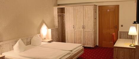 Un dormitorio con cama de madera, un armario, un escritorio con lámpara y una puerta con un cartel.